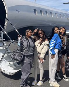 four women standing in front of an airplane with the door open and one woman taking a selfie