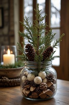 a glass jar filled with pine cones and balls on top of a wooden table next to a candle