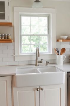 White farmhouse sink under a window in a kitchen with white cabinetry and a white tile backsplash. Mid Century Modern Bedroom Colors, Farmhouse Cabinets