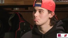 a young man wearing a red and black hat in a locker room with other sports equipment