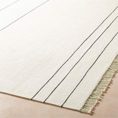 a white rug with black lines on the bottom and fringes in the middle, sitting on a beige floor