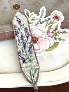 a beaded sticker sitting on top of a wooden table next to a flower