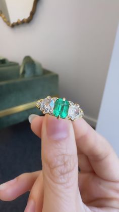 a person holding an emerald and diamond ring