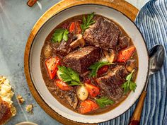 a bowl of stew with meat and vegetables in it on a table next to bread