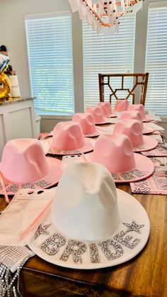 a table topped with pink hats on top of place mats and napkins next to a chandelier