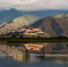 the potala palace sits on top of a hill overlooking a body of water with mountains in the background