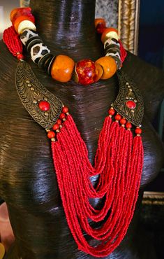 Here's a Bohemian Necklace and Bib Set I found in my inventory. The longer strand is a vintage piece that I did not make. It measures a non-adjustable 28" and closes with a button and a loop. Multiple strands of red-orange seed beads comprise the majority of the piece and two ornate metal accents (looks like bronze) are symmetrically set on each side with an orange-red cabochon (jade??). The shorter necklace is one that I made. It measures a non-adjustable 19" and features the following components: Tibetan resin, Moroccan resin, Zebu bone*, gold tone metal spacers, vintage Chinese brass coins, red branch corals, vintage brass beads and round tiger's eye. Closes with a gold tone hook and eye. Pair them together, or wear separately. These also will mix and match well with your personal favor Vintage Red Jewelry With Dangling Beads, Hand-strung Necklaces For Festivals, Vintage Adjustable Jewelry With Dangling Beads, Bohemian Hand-strung Necklaces For Festivals, Bohemian Festival Hand-strung Necklaces, Vintage Polished Beads Necklaces, Unique Hand-strung Multi-strand Necklace, Adjustable Artisan Beads With Dangling Details, Adjustable Large Beads Jewelry For Rituals