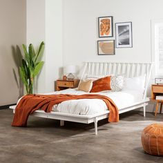 a white bed sitting in a bedroom on top of a hard wood floor next to a potted plant