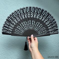 a hand holding an ornate black fan against a blue wall