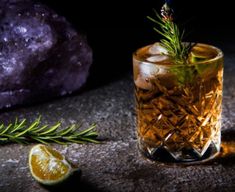 an alcoholic drink with rosemary garnish on the rocks