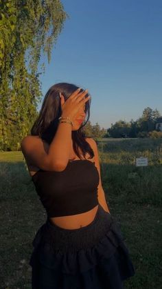 a woman standing in the grass covering her face with her hands and looking into the distance