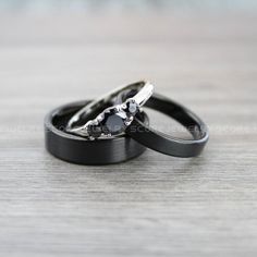 two wedding rings with black diamonds on them sitting on top of each other in front of a wooden table