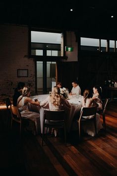 a group of people sitting around a table in a room with wooden floors and windows