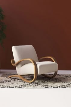 a white rocking chair sitting on top of a rug next to a potted plant