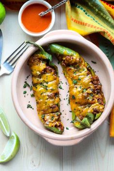 two stuffed peppers in a bowl next to some dipping sauce and limes on the side