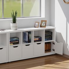 a white book shelf with books and pictures on it in front of a large window