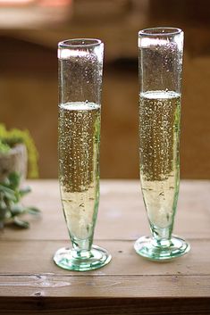 two champagne flutes sitting on top of a wooden table next to each other with bubbles in them