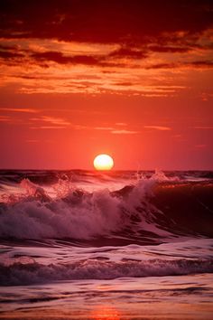 the sun is setting over the ocean with waves crashing in front of it and red clouds