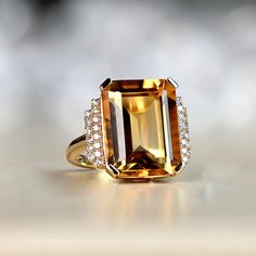 This ring features an 11.35 carat emerald-cut, prong-set natural citrine. Flanking the center stone are two steps of round brilliant cut diamonds set on the shoulders. Adorning the under-gallery is intricate openwork. This ring is handcrafted in 18k yellow gold.
The measurements of the center stone are approximately 16.00mm x 12.06mm x 7.80mm.
This ring can be resized to any finger size at no additional cost.
If you have any questions regarding the Springs Ring, please feel free to contact us. Citrine Engagement Ring, Estate Diamond Jewelry, Emerald Cut Engagement, Elegant Engagement Rings, Emerald Engagement Ring Cut, Yellow Gold Engagement, Citrine Ring, Citrine Stone, 18k Yellow Gold Ring