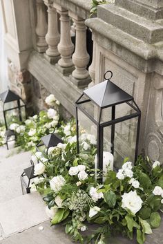 white flowers and greenery are on the ground next to a black lantern outside an old building