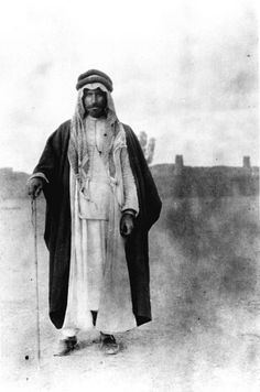 an old black and white photo of a man dressed in traditional garb, holding a cane