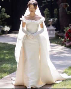 a woman in a white wedding gown and veil is standing on the sidewalk with her hands behind her back