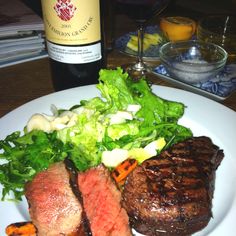 steak, lettuce and carrots on a plate next to a bottle of wine