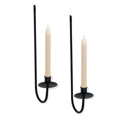 two black candles are next to each other on a white background, one is lit and the other is turned off