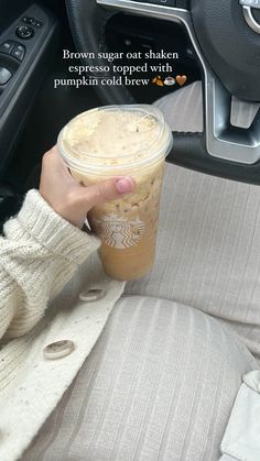 a woman holding a cup of coffee in her hand while sitting in the driver's seat of a car