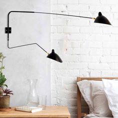 two black lamps are hanging on the wall next to a bed with white sheets and pillows