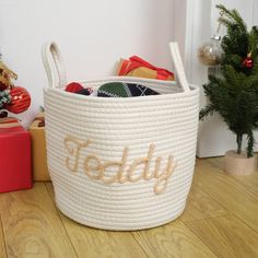 a white basket with the word teddy written on it next to presents and christmas trees