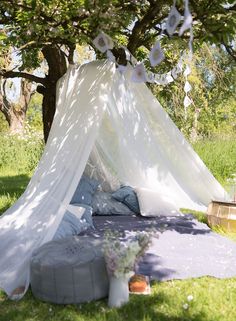 a white tent is set up in the grass under a tree with flowers on it