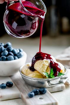 someone pouring ice cream into a bowl filled with blueberries and raspberry sauce