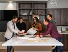 four people standing around a kitchen island in front of a counter top with papers on it