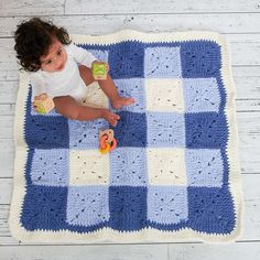 a small child laying on top of a blue and white checkerboard afghan blanket