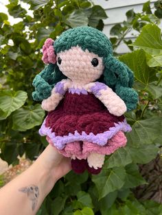 a crocheted doll in a dress is held up by someone's hand