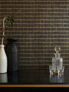 two vases sitting on top of a wooden table next to a wallpapered wall