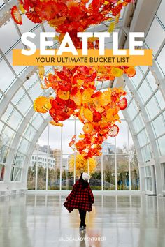 a person in a red and black coat is standing under a colorful sculpture with the words seattle your ultimate bucket list