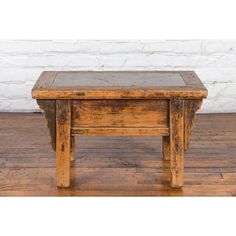 an old wooden table sitting on top of a hard wood floor next to a white brick wall