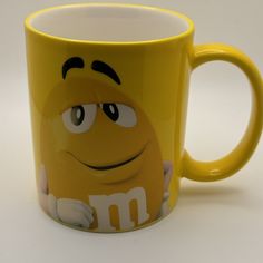 a yellow coffee mug with m & m's on the side and eyes painted on it