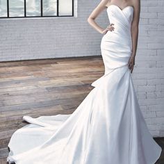 a woman in a white wedding dress standing on a wooden floor next to a brick wall