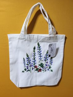 a white tote bag with blue and purple flowers painted on the side, sitting on a yellow surface