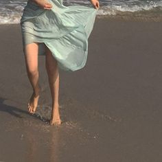 a woman in a blue dress is walking on the beach