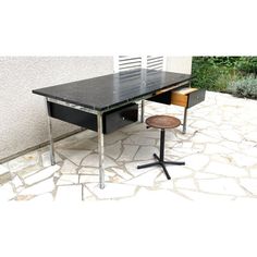 a black desk with two drawers and a chair next to it on a stone patio