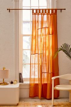 an orange sheer curtain hangs in front of a window with a chair and potted plant