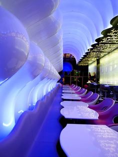 rows of white tables and chairs are lined up in a room with blue lights on the ceiling