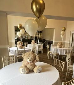 a teddy bear sitting on top of a table with balloons in the air above it