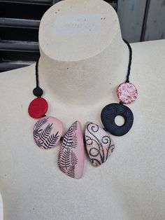 a white mannequin wearing a pink and black necklace with three different designs on it