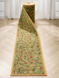 a green rug with red flowers on it in front of a white curtained window