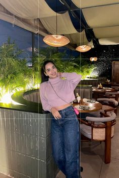 a woman standing next to a counter in front of a plant filled wall with hanging lights